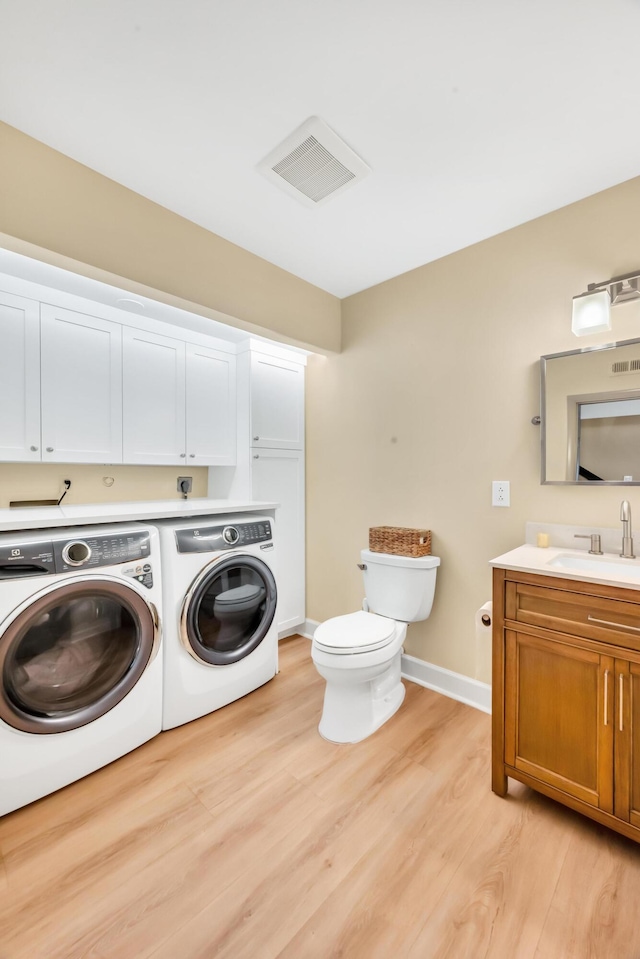 clothes washing area featuring light wood-type flooring, separate washer and dryer, and sink