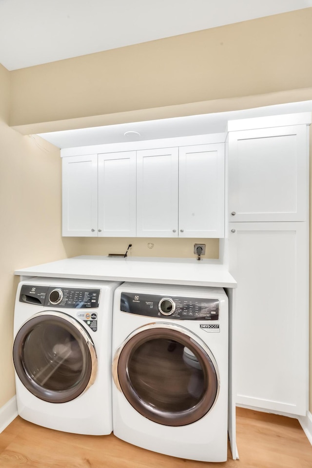 washroom with washer and dryer, cabinets, and light hardwood / wood-style flooring