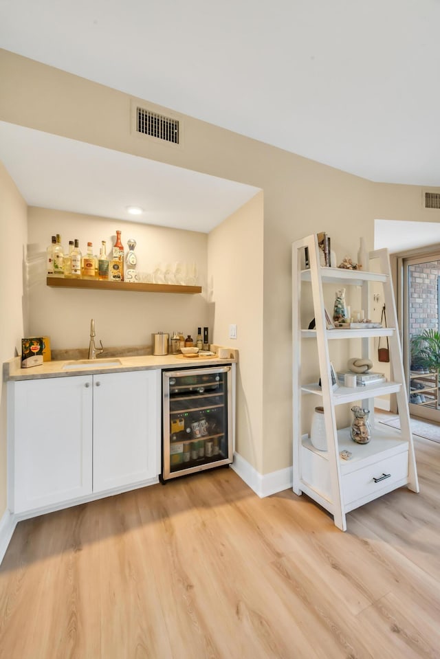 bar with sink, white cabinets, beverage cooler, and light hardwood / wood-style floors