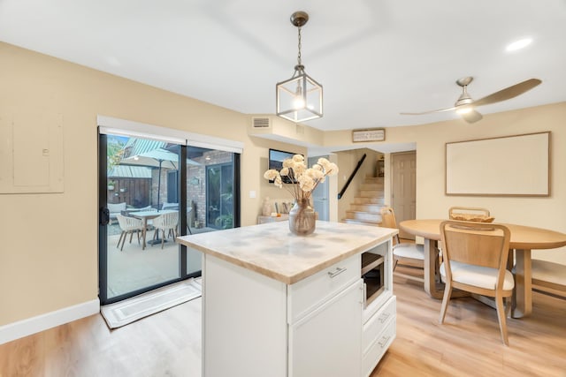 kitchen with white cabinetry, stainless steel microwave, a center island, light hardwood / wood-style flooring, and pendant lighting