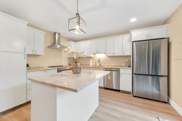 kitchen with appliances with stainless steel finishes, wall chimney range hood, light hardwood / wood-style flooring, white cabinets, and a kitchen island