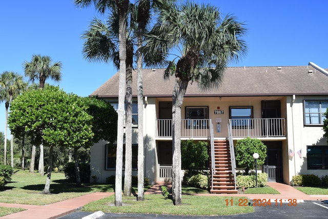 view of front facade featuring stairway, stucco siding, a front yard, and roof with shingles