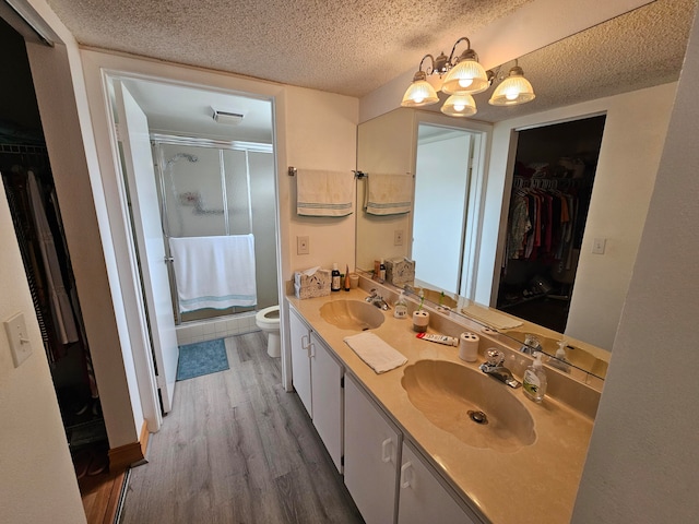 bathroom featuring an enclosed shower, vanity, a textured ceiling, hardwood / wood-style flooring, and toilet