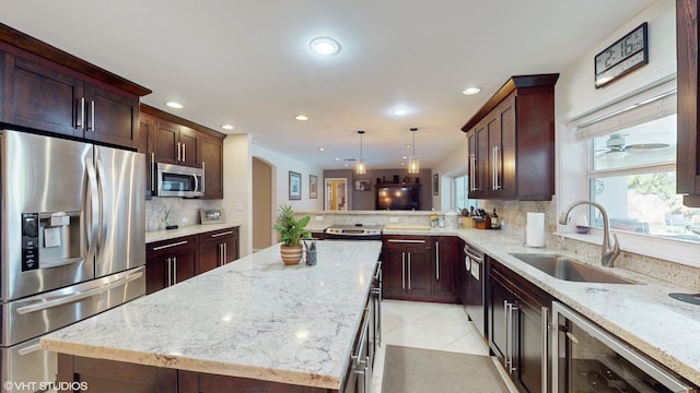 kitchen featuring sink, a center island, hanging light fixtures, stainless steel appliances, and light stone counters