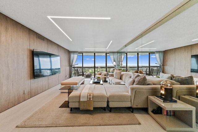 living room featuring a wealth of natural light, light hardwood / wood-style flooring, floor to ceiling windows, and wood walls