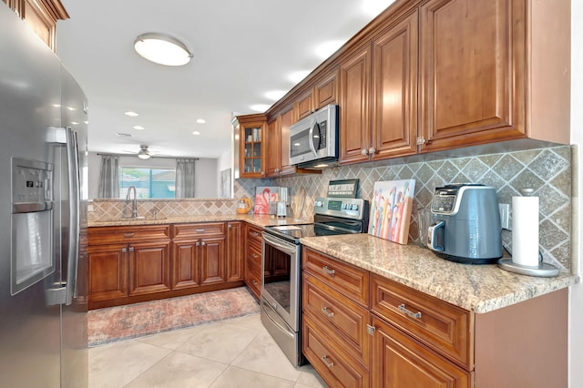 kitchen with sink, stainless steel appliances, light stone counters, backsplash, and light tile patterned floors