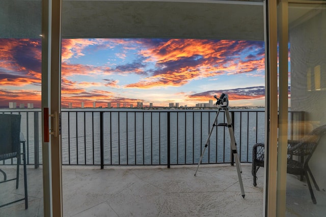 balcony at dusk featuring a water view