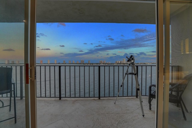 balcony at dusk featuring a water view