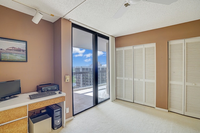 office space with floor to ceiling windows, ceiling fan, rail lighting, light colored carpet, and a textured ceiling