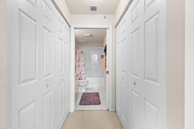 hall featuring light tile patterned floors and a textured ceiling