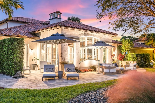 back house at dusk with outdoor lounge area and a patio area