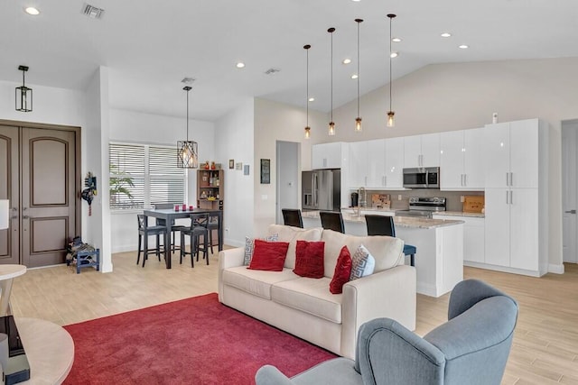 living room with sink, light hardwood / wood-style flooring, high vaulted ceiling, and an inviting chandelier