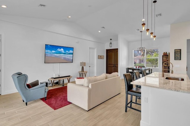 living room featuring sink, an inviting chandelier, vaulted ceiling, and light wood-type flooring