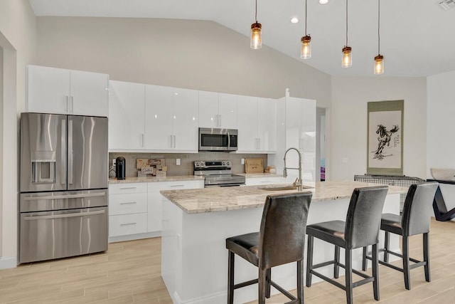 kitchen with sink, an island with sink, decorative light fixtures, white cabinets, and appliances with stainless steel finishes