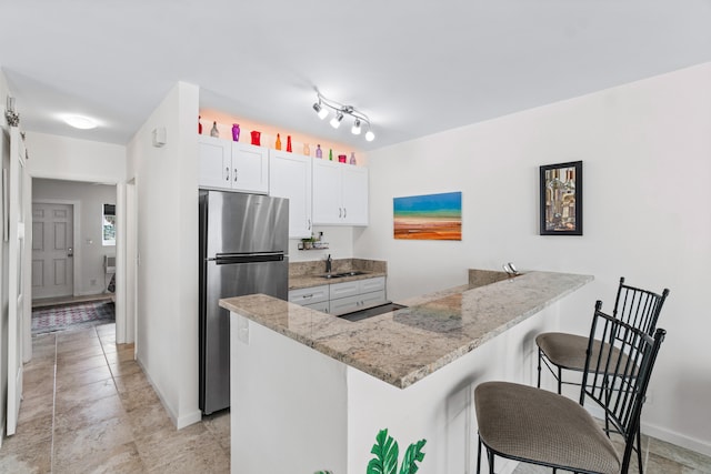 kitchen featuring kitchen peninsula, stainless steel fridge, white cabinetry, and a kitchen breakfast bar