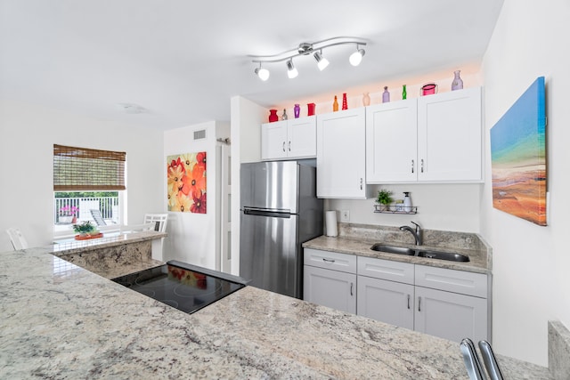 kitchen featuring stainless steel fridge, sink, white cabinetry, and light stone counters