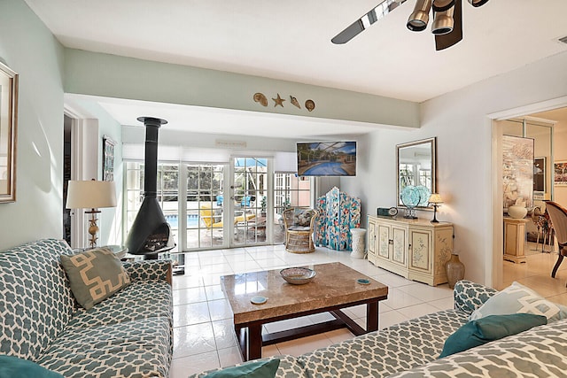 living room with a wood stove, ceiling fan, and light tile patterned flooring