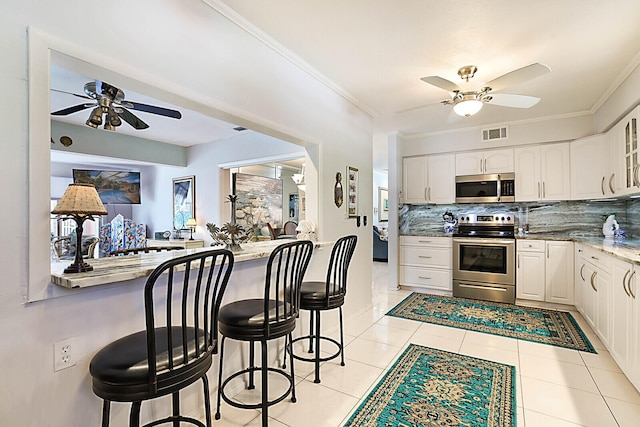 kitchen featuring appliances with stainless steel finishes, a kitchen breakfast bar, crown molding, light tile patterned floors, and white cabinetry