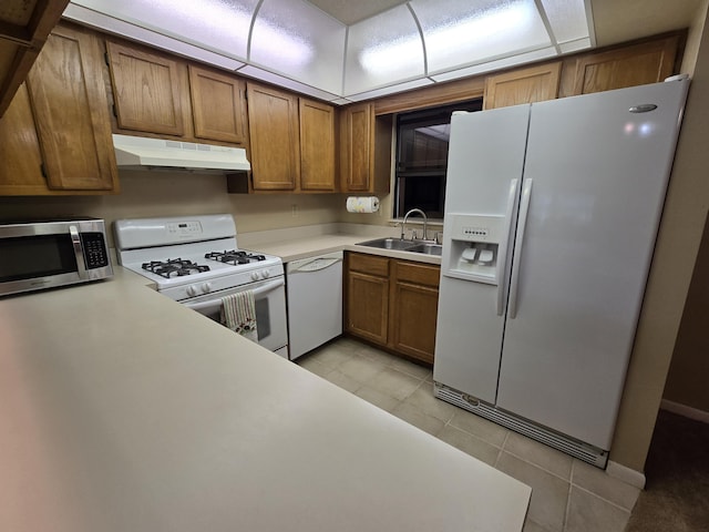 kitchen featuring under cabinet range hood, white appliances, a sink, light countertops, and brown cabinetry