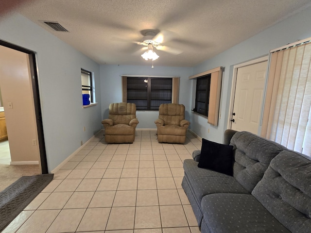 living room featuring baseboards, visible vents, a ceiling fan, a textured ceiling, and light tile patterned flooring