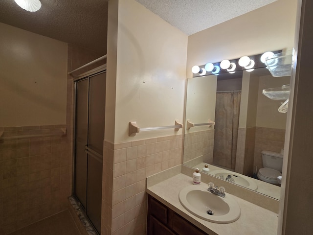 full bath featuring tile walls, a wainscoted wall, a textured ceiling, and a shower stall