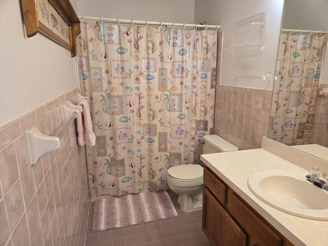 full bath with a wainscoted wall, tile walls, toilet, vanity, and tile patterned flooring