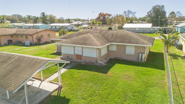 rear view of house featuring a residential view, roof with shingles, a lawn, and stucco siding