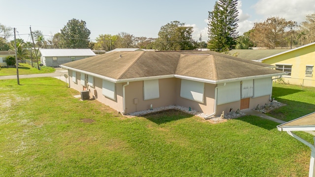 back of property with central AC, a shingled roof, a lawn, and stucco siding