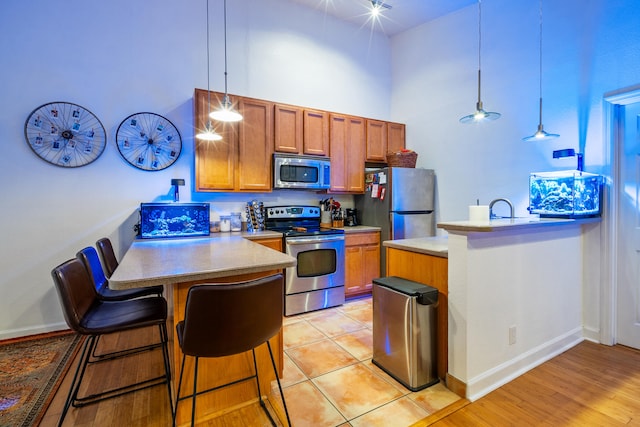 kitchen featuring pendant lighting, a kitchen breakfast bar, light hardwood / wood-style flooring, a towering ceiling, and appliances with stainless steel finishes