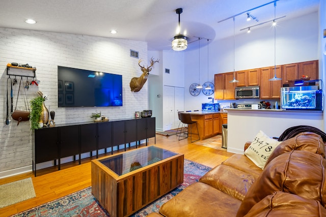 living room with brick wall, a textured ceiling, ceiling fan, high vaulted ceiling, and light hardwood / wood-style flooring