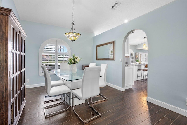 dining space with a textured ceiling, vaulted ceiling, and dark wood-type flooring