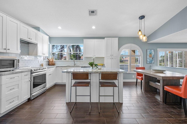 kitchen featuring light stone counters, hanging light fixtures, stainless steel appliances, and lofted ceiling