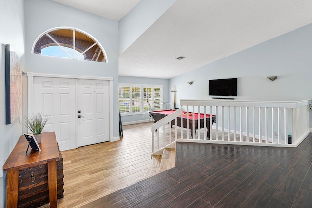 foyer with lofted ceiling, wood finish floors, visible vents, and baseboards