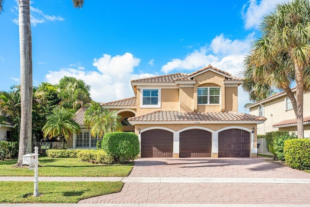 mediterranean / spanish-style house with a garage, decorative driveway, a tiled roof, and stucco siding