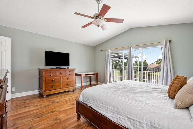 bedroom featuring access to exterior, vaulted ceiling, baseboards, and wood finished floors