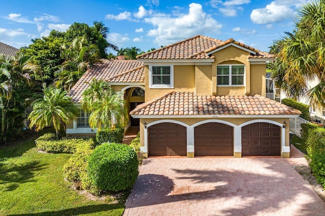 mediterranean / spanish-style house featuring an attached garage, a tiled roof, a front yard, and stucco siding