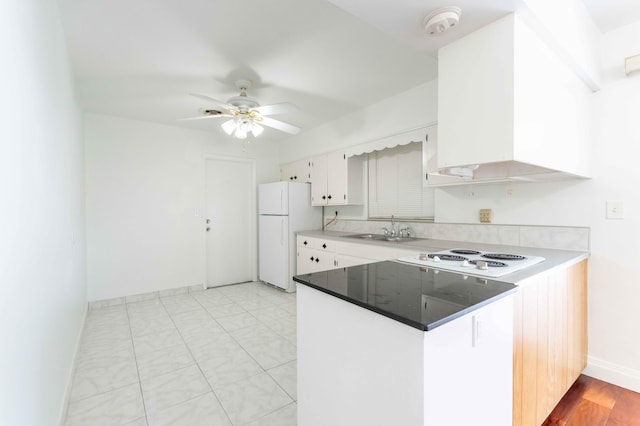 kitchen featuring white appliances, white cabinets, wall chimney range hood, sink, and ceiling fan