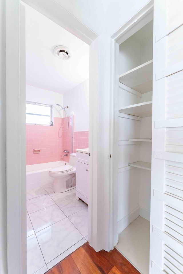 full bathroom with vanity, tiled shower / bath, toilet, tile walls, and wood-type flooring