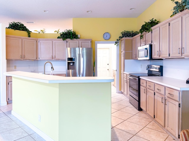 kitchen with appliances with stainless steel finishes, light brown cabinetry, and an island with sink