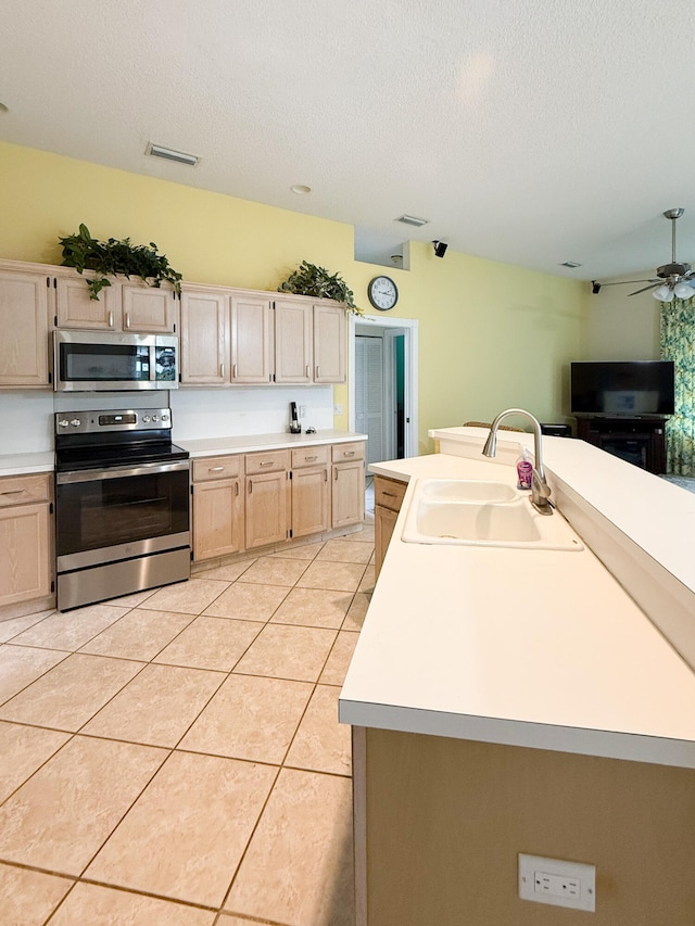 kitchen with sink, light brown cabinets, stainless steel appliances, a textured ceiling, and a kitchen island with sink