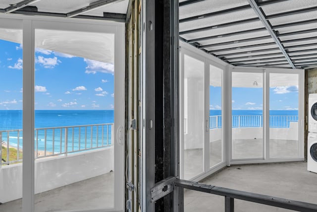 unfurnished sunroom with a beach view, stacked washing maching and dryer, a healthy amount of sunlight, and a water view