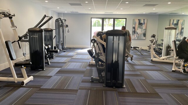 exercise room with a paneled ceiling and dark carpet