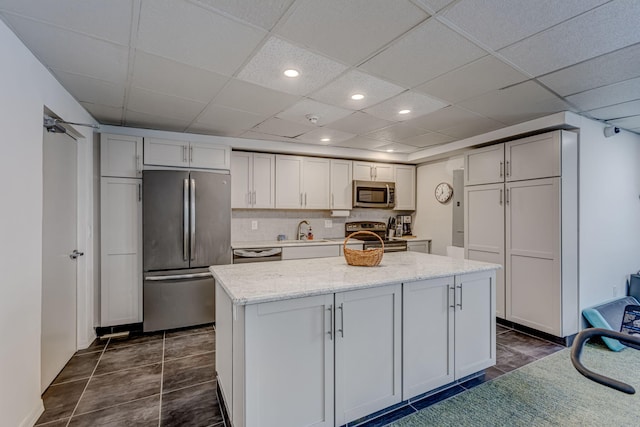 kitchen featuring light stone countertops, appliances with stainless steel finishes, decorative backsplash, sink, and a kitchen island