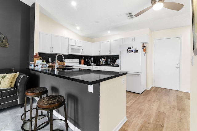 kitchen with kitchen peninsula, a breakfast bar, white cabinets, and white appliances