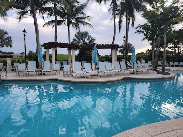 pool at dusk featuring a pergola and a patio area