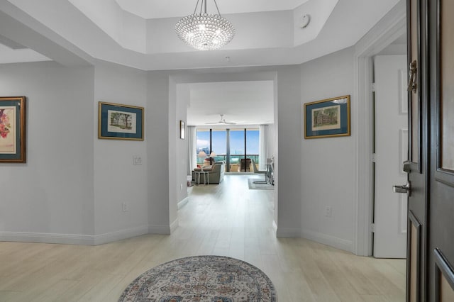 hallway featuring a chandelier, floor to ceiling windows, a raised ceiling, and light hardwood / wood-style flooring