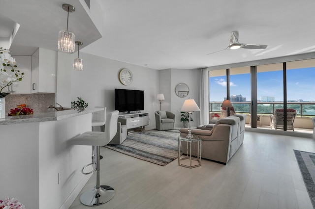 living room featuring light hardwood / wood-style flooring, expansive windows, ceiling fan with notable chandelier, and sink