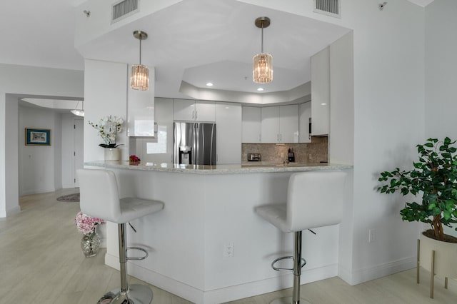 kitchen featuring kitchen peninsula, stainless steel fridge, a breakfast bar, and white cabinets