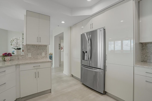 kitchen with decorative backsplash, stainless steel fridge, light stone counters, and white cabinetry