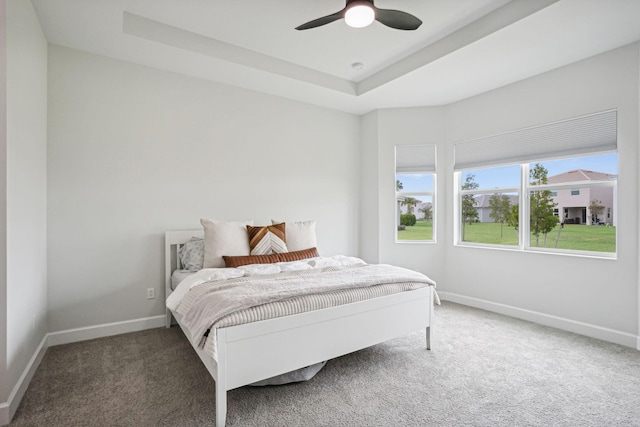 carpeted bedroom featuring ceiling fan and a raised ceiling